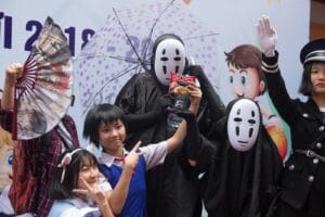 Group of people in cosplay costumes posing at an anime-themed celebration with props and masks.