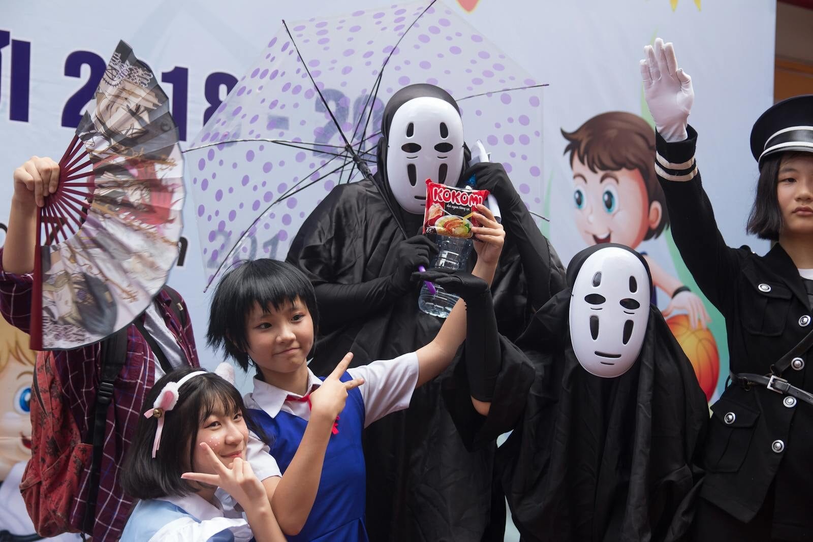 Group of people in cosplay costumes posing at an anime-themed celebration with props and masks.