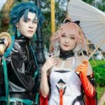 Two cosplayers in vibrant costumes posing with a parasol outdoors.