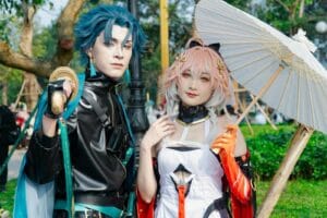Two cosplayers in vibrant costumes posing with a parasol outdoors.