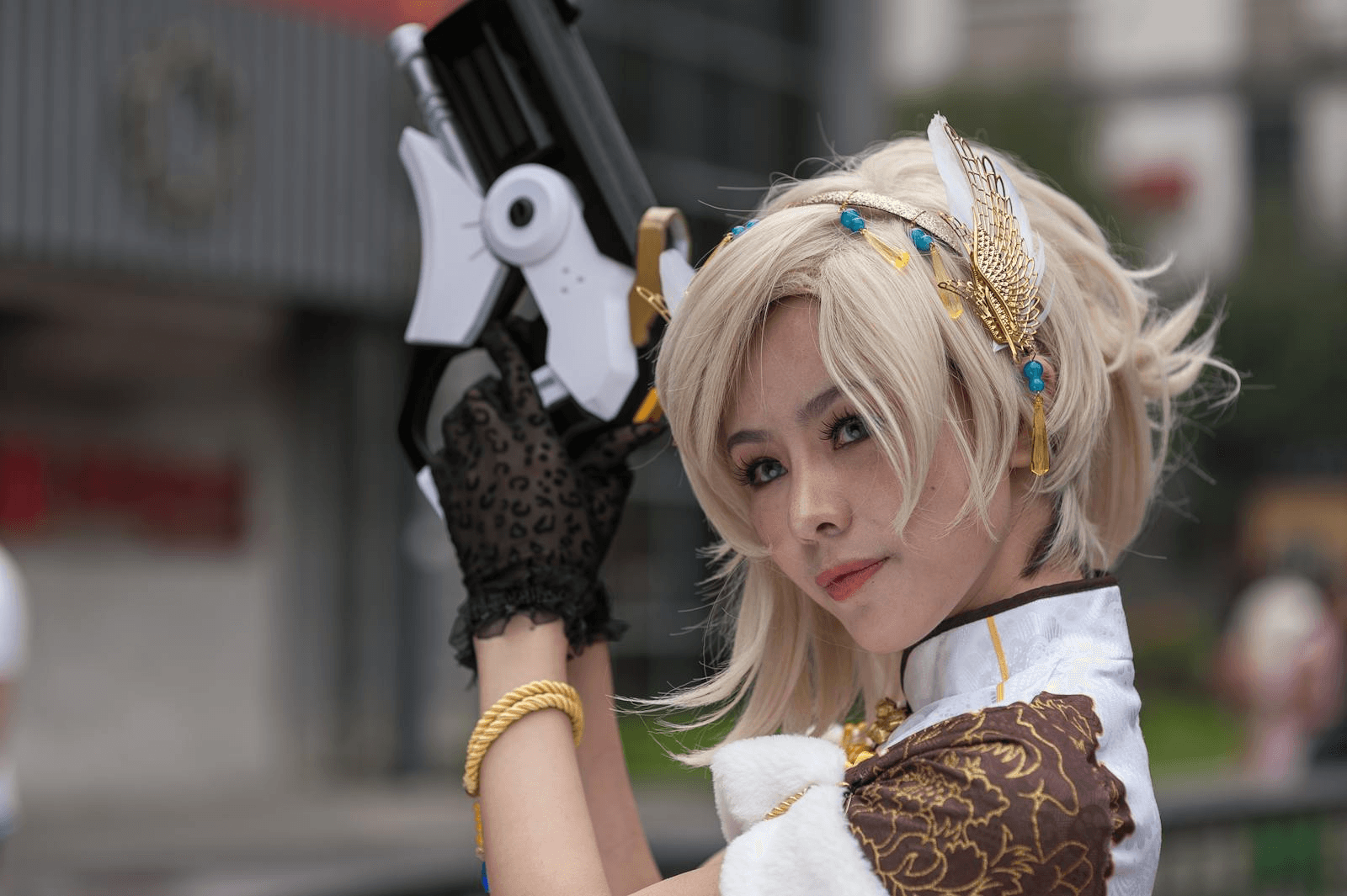 Cosplayer With Intricate Costume And Prop Gun, Posing Outdoors During The Day.