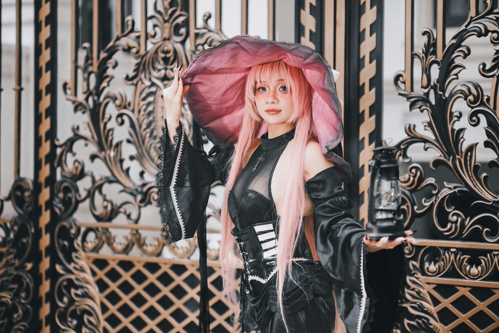 A stunning cosplay witch with pink hair holding a lantern by an intricate gate.