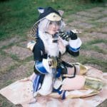Cosplayer posing in elaborate fantasy outfit with animal ears and gold armor sitting on a blanket.