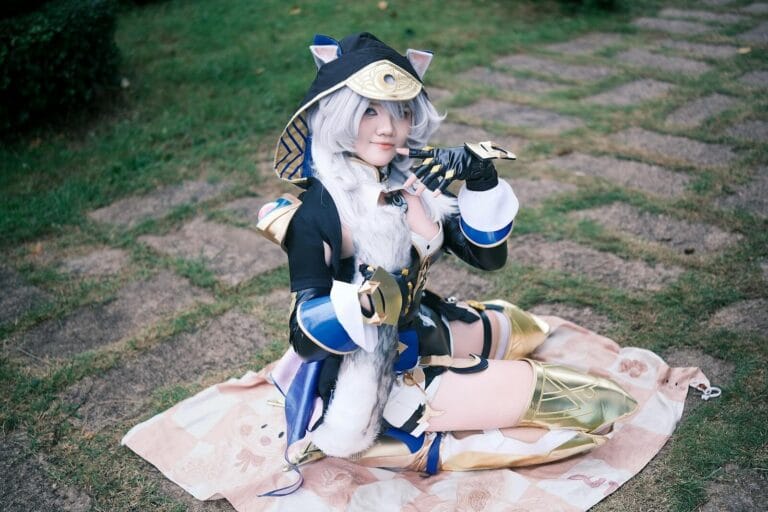Cosplayer Posing In Elaborate Fantasy Outfit With Animal Ears And Gold Armor Sitting On A Blanket.