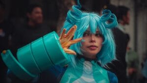 Cosplayer in blue wig and costume striking a pose at an outdoor event.