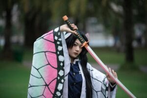 A cosplay character poses with a sword outdoors, displaying intricate costume design.