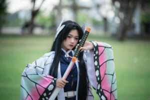 Cosplayer dressed as a character holding a sword in a park setting.