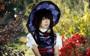A woman in a detailed witch cosplay outfit stands amidst colorful fall foliage, showcasing her elaborate costume design.