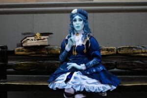 A cosplayer in a blue costume posed on a bench with a fantasy book, creating a whimsical scene.