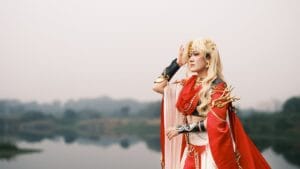 A person in fantasy costume poses by a serene lake, showcasing detailed cosplay attire.